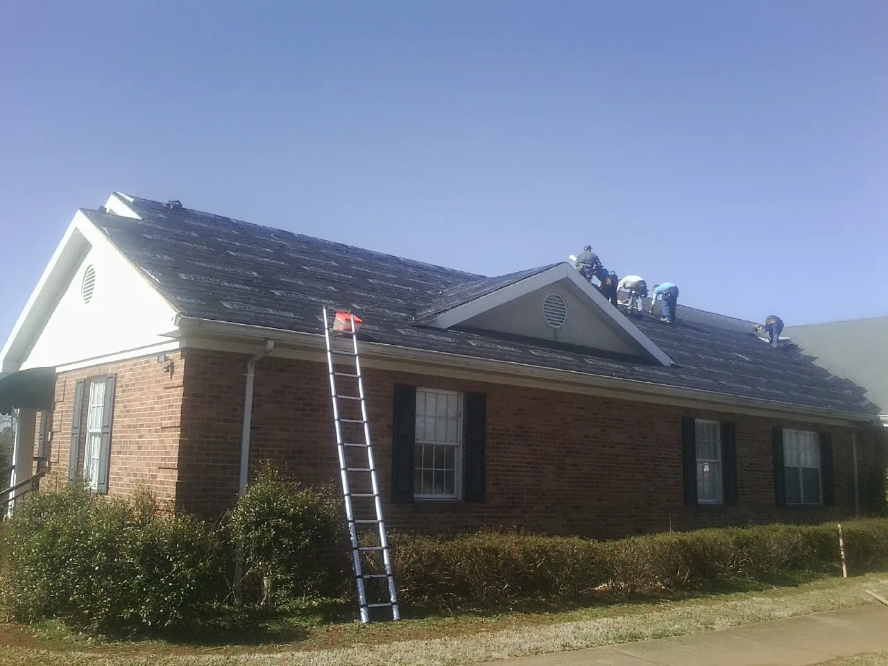 Crew tearing shingles off a brick ranch roof with a ladder set — Metal Roof Repair work by our crew in Jersey Mills