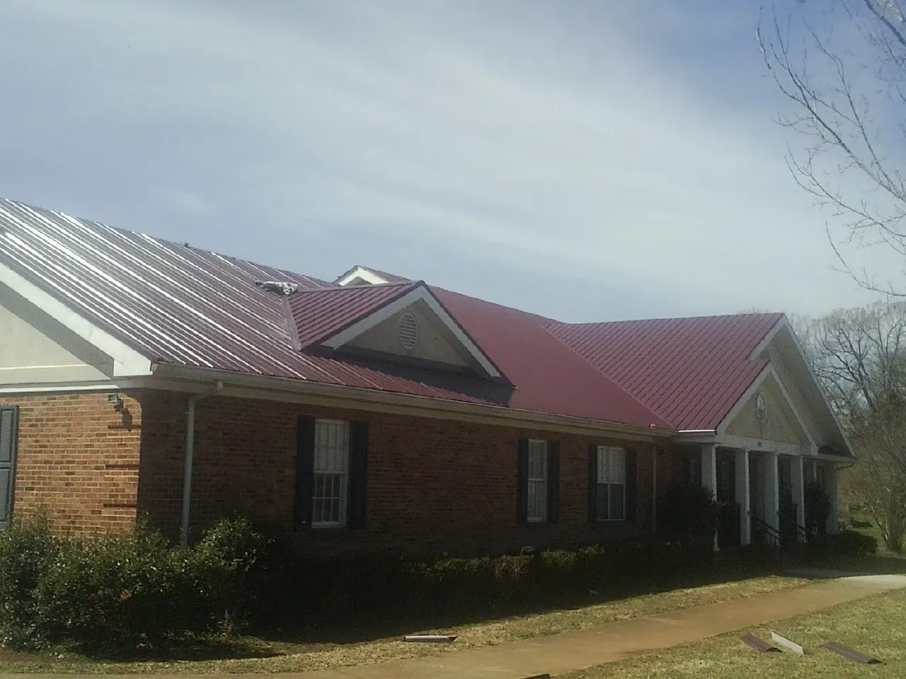 Red metal roof with gabled entries on a long brick building, from a Hail Damage Roof Repair job in Jersey Mills