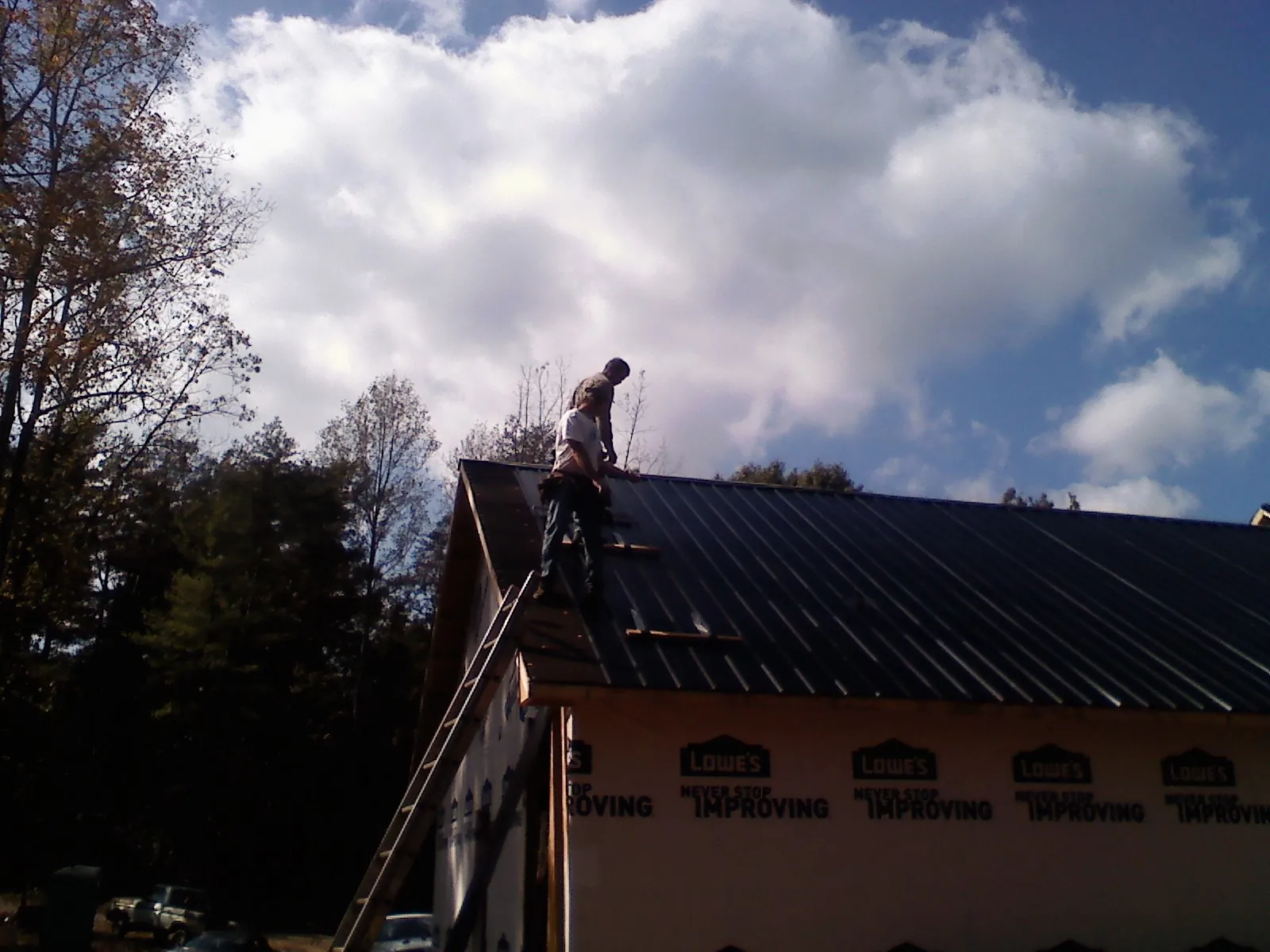 Roofer fastening dark metal panels high against a cloudy sky, from a Roof Inspection job in Jersey Mills