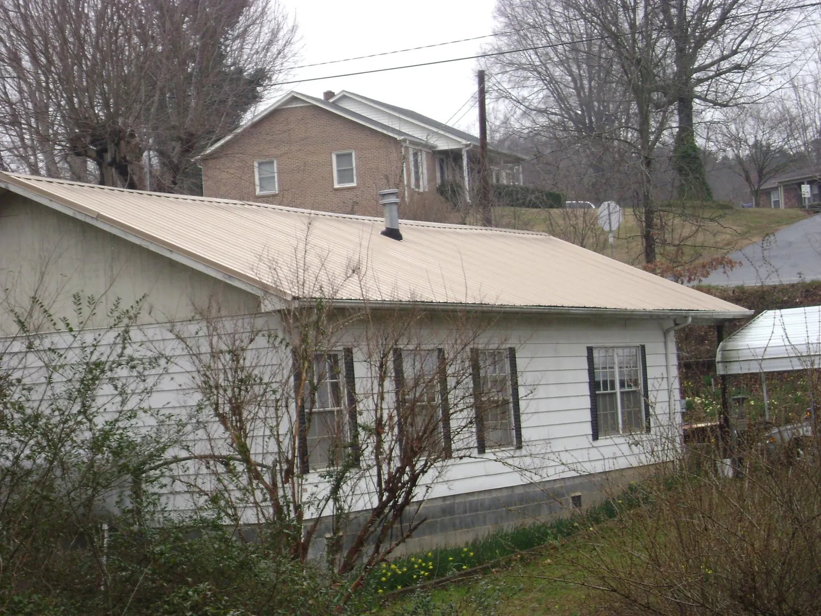 Tan metal roof on a white sided house set into a hillside — Commercial Roofing by Roofing Brothers in Jersey Mills